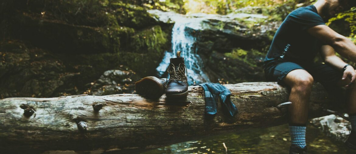 a pair of hiking boots and hiking socks on top of a log with a flowing waterfall in the background