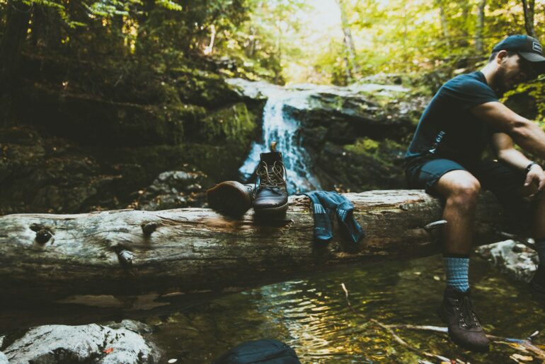 a pair of hiking boots and hiking socks on top of a log with a flowing waterfall in the background