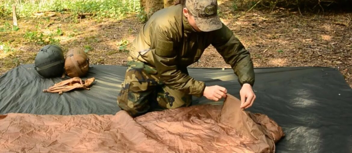 a man in a military uniform showing off the snugpak sleeping bag features