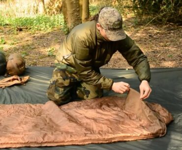 a man in a military uniform showing off the snugpak sleeping bag features