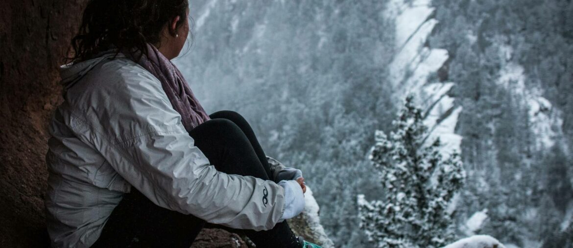 woman sitting on a mountain in winter, choosing womens hiking trousers for summer and winter