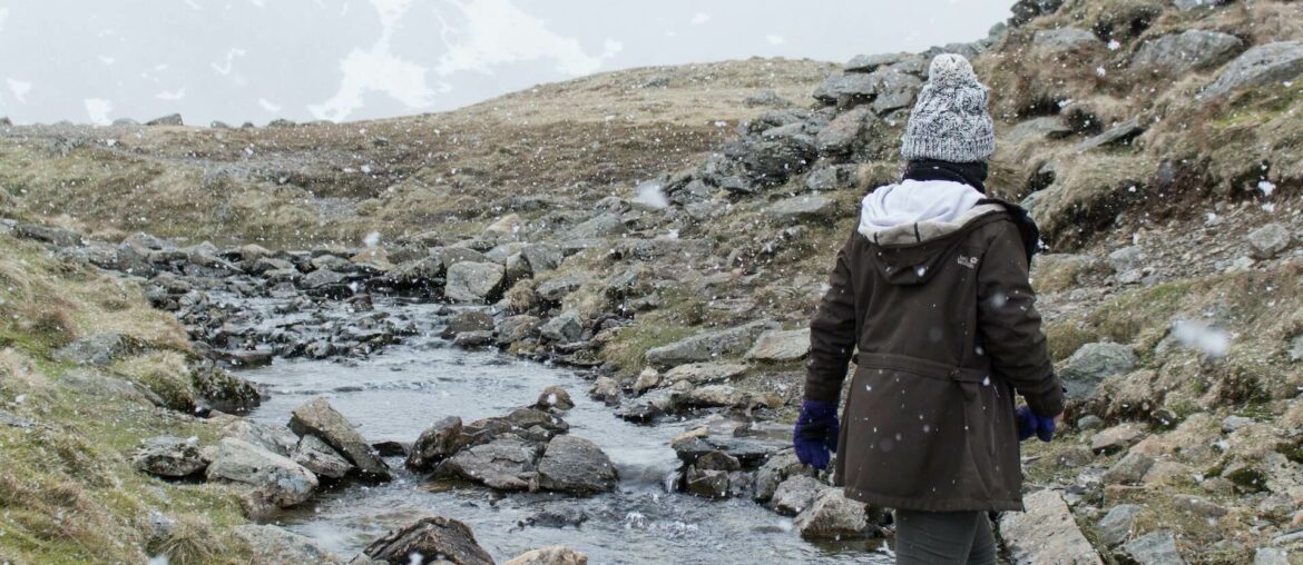 Woman walking through a stream in the rain showcasing water resistant vs waterproof women's hiking trousers