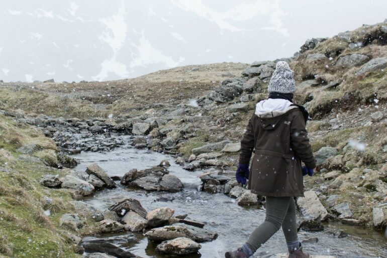 Woman walking through a stream in the rain showcasing water resistant vs waterproof women's hiking trousers