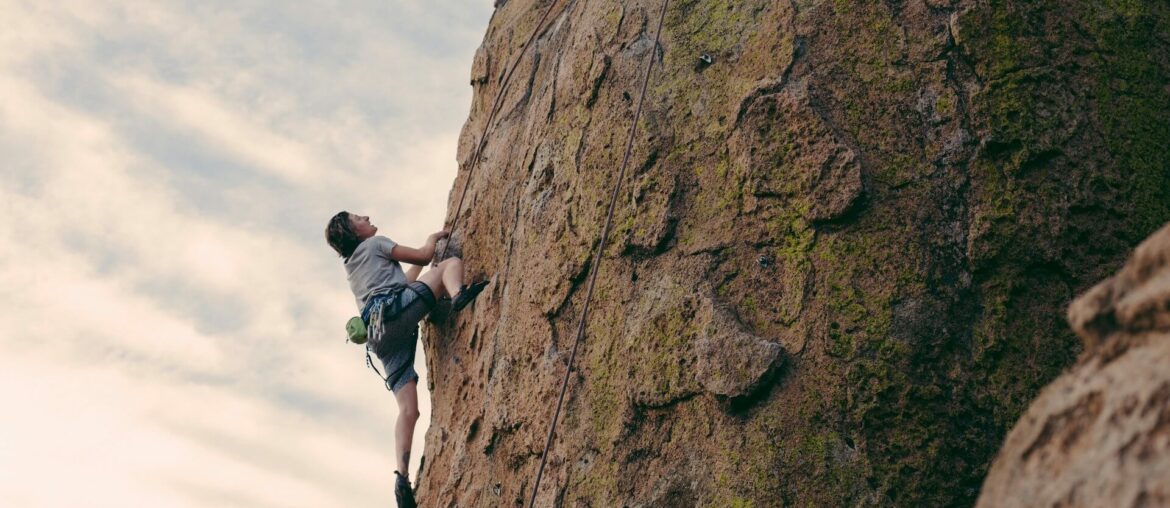What to Wear for Indoor vs Outdoor Rock Climbing Person climbing a rock face after deciding what to wear for indoor vs outdoor rock climbing
