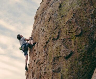 Person climbing a rock face after deciding what to wear for indoor vs outdoor rock climbing