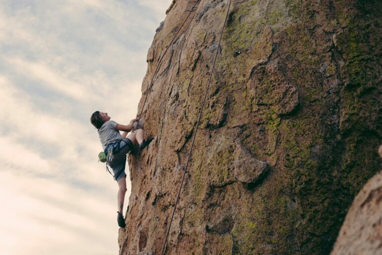 Person climbing a rock face after deciding what to wear for indoor vs outdoor rock climbing